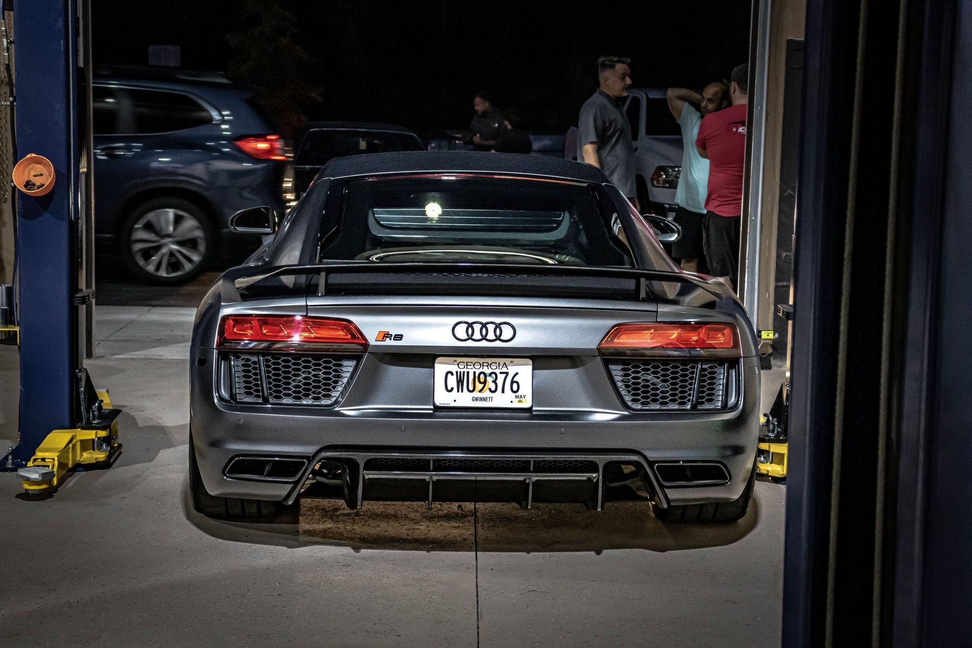 A gray audi r8 is parked on a lift in a garage.