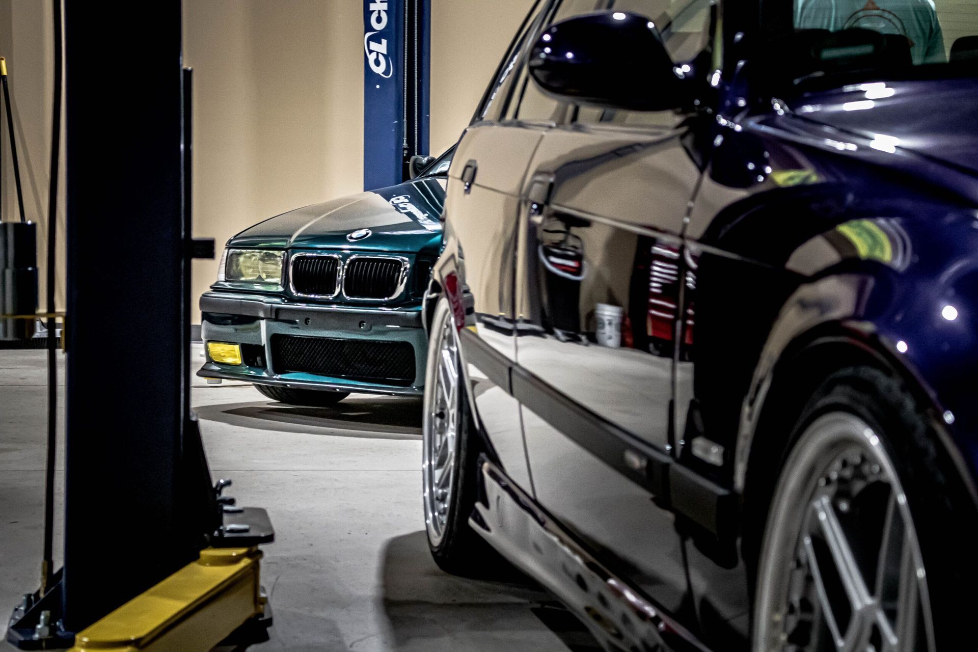 A bmw is sitting on a lift in a garage next to another car.
