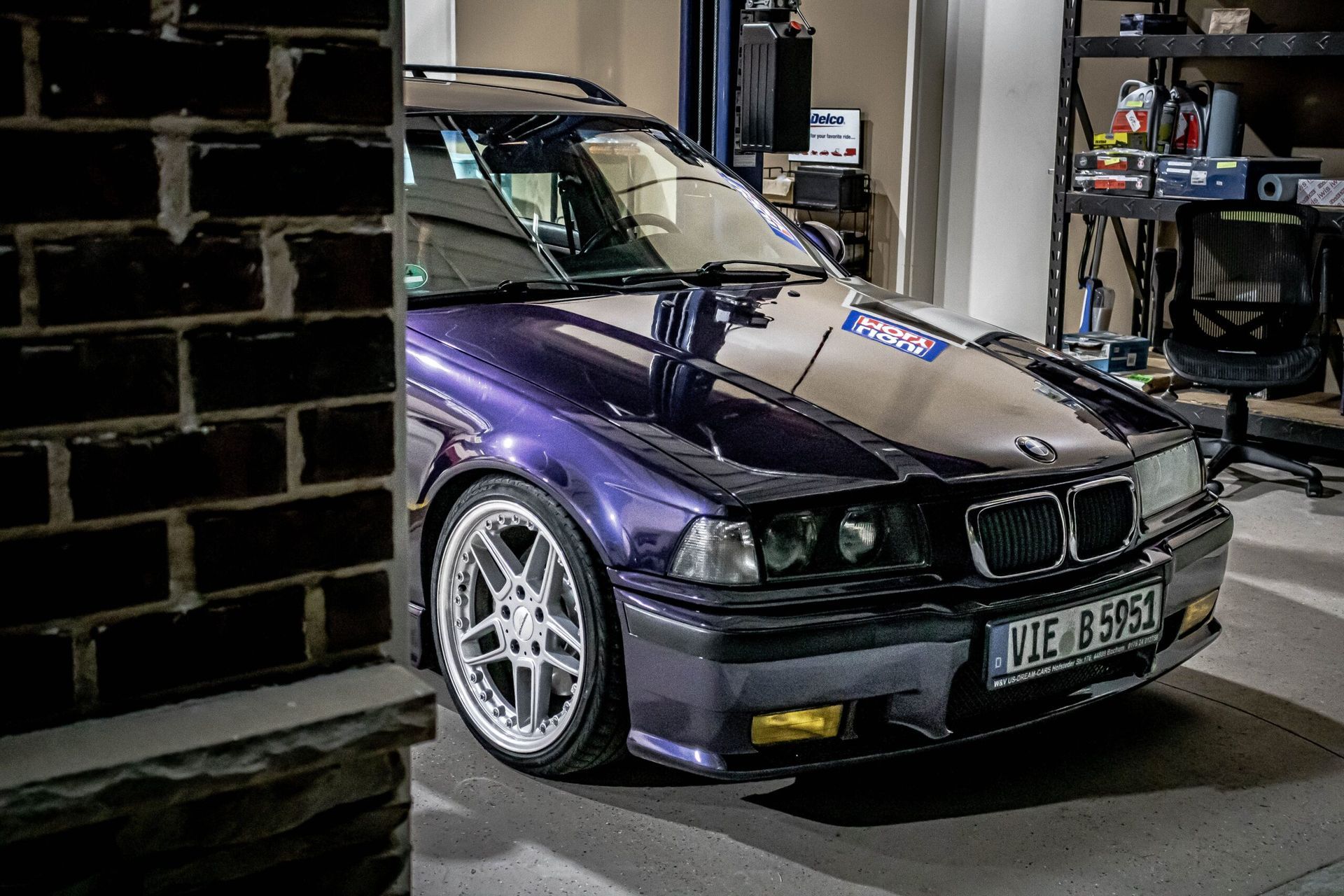 A purple bmw is parked in a garage next to a brick wall.