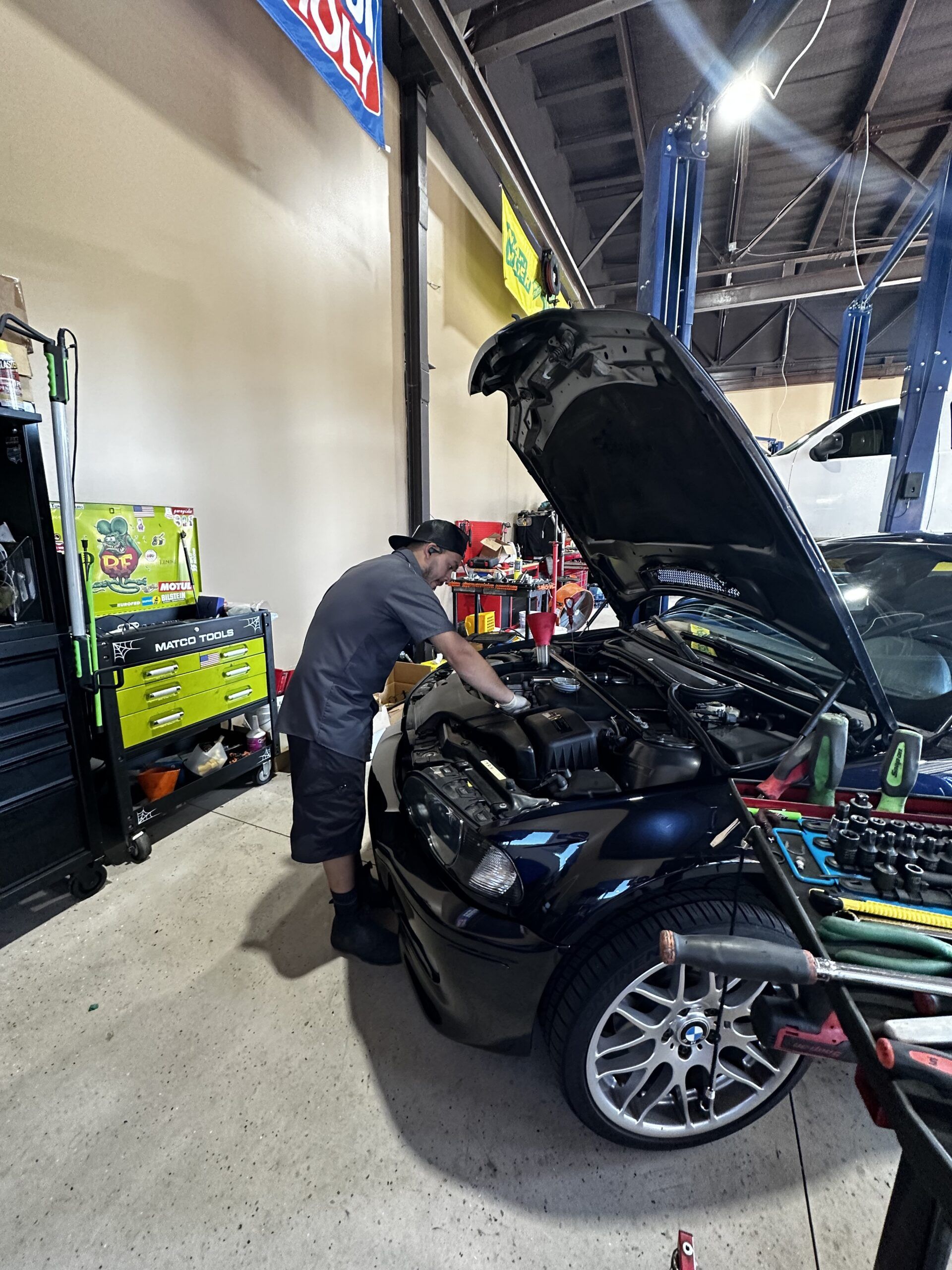 A man is working on a car in a garage with the hood open.