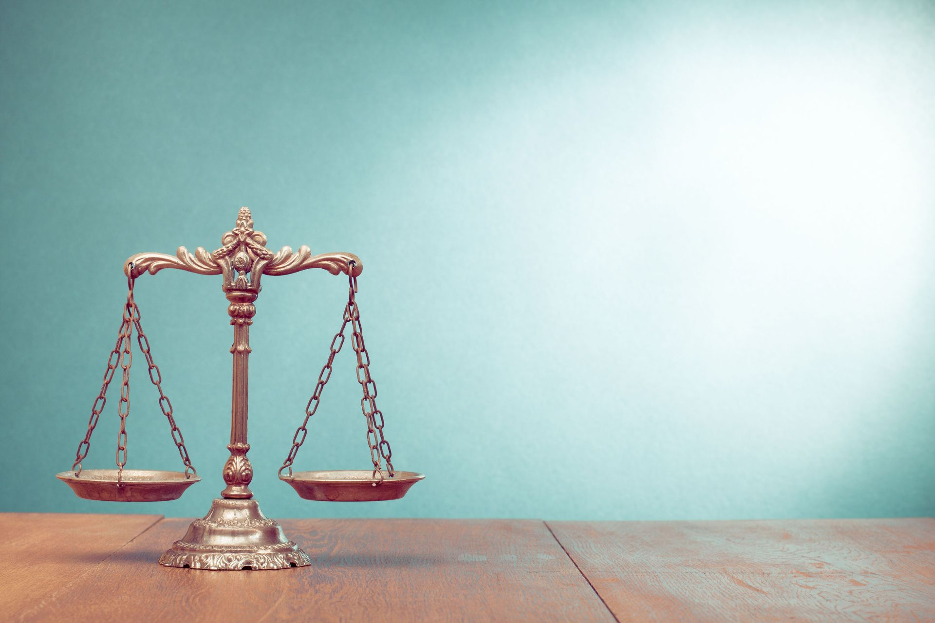 Gold balance scales on a wooden surface against a teal background, symbolizing justice.