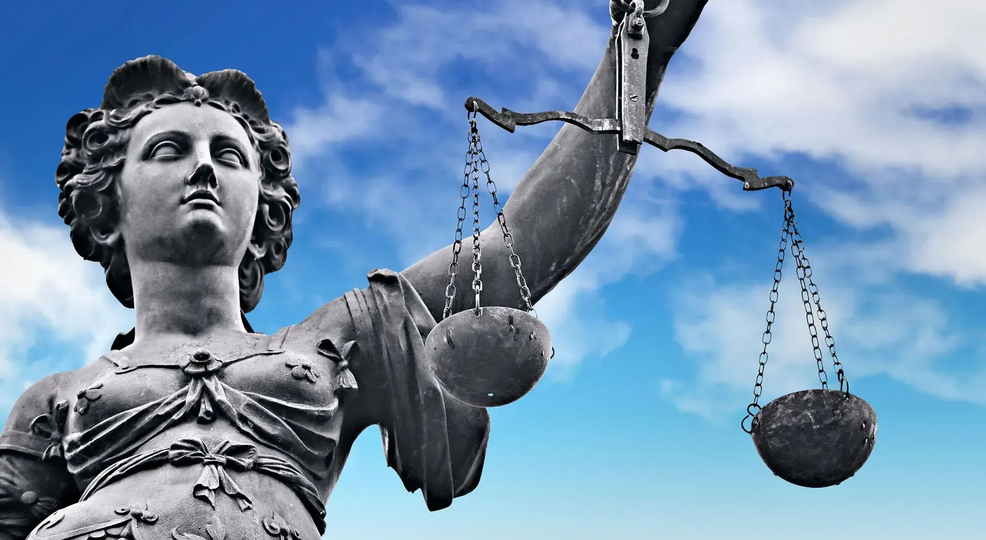 Statue of Lady Justice holding scales, against a blue sky with clouds.