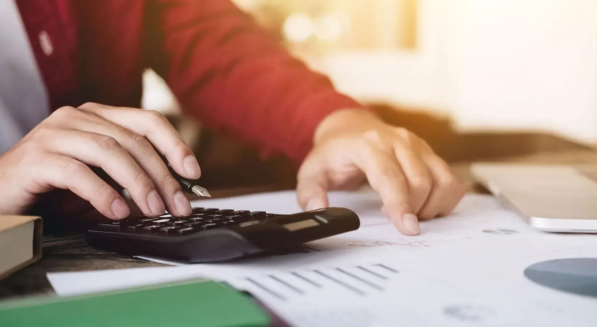 Person using a calculator with paperwork on a desk. Focus on hands and device.