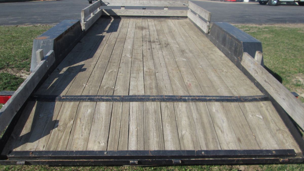 A wooden trailer is sitting on the grass in a parking lot.