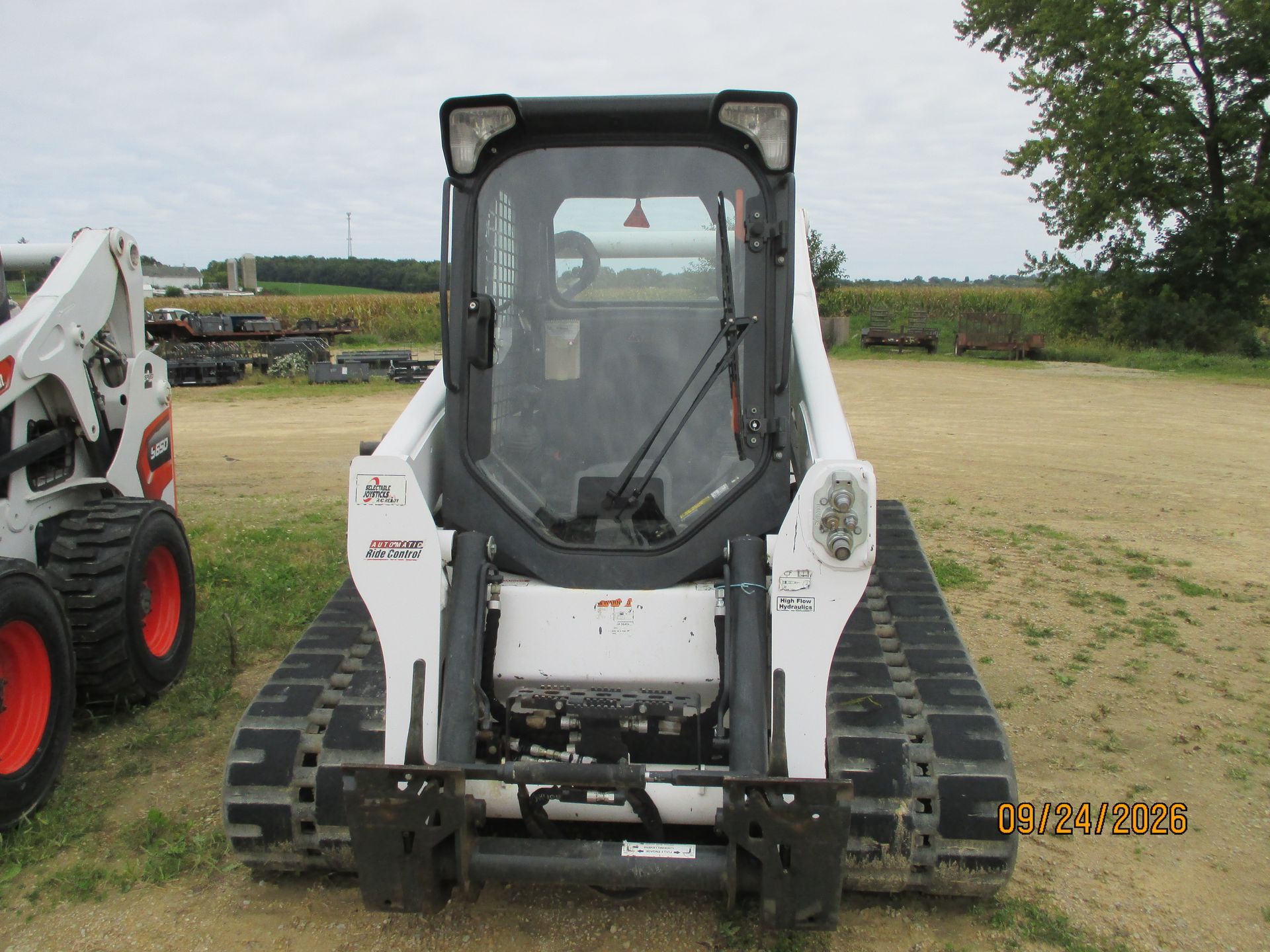 White tracked skid steer loader facing camera on a grassy field with a partial red machine at left