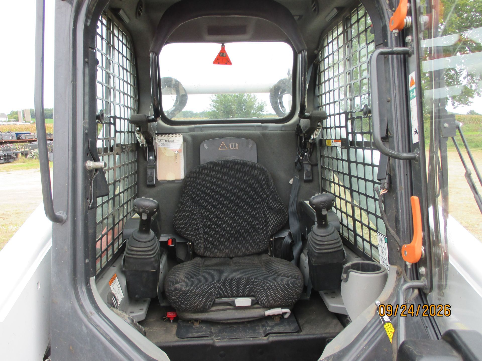 Interior of a compact construction vehicle cab with a black seat, controls, and safety grilles on the windows