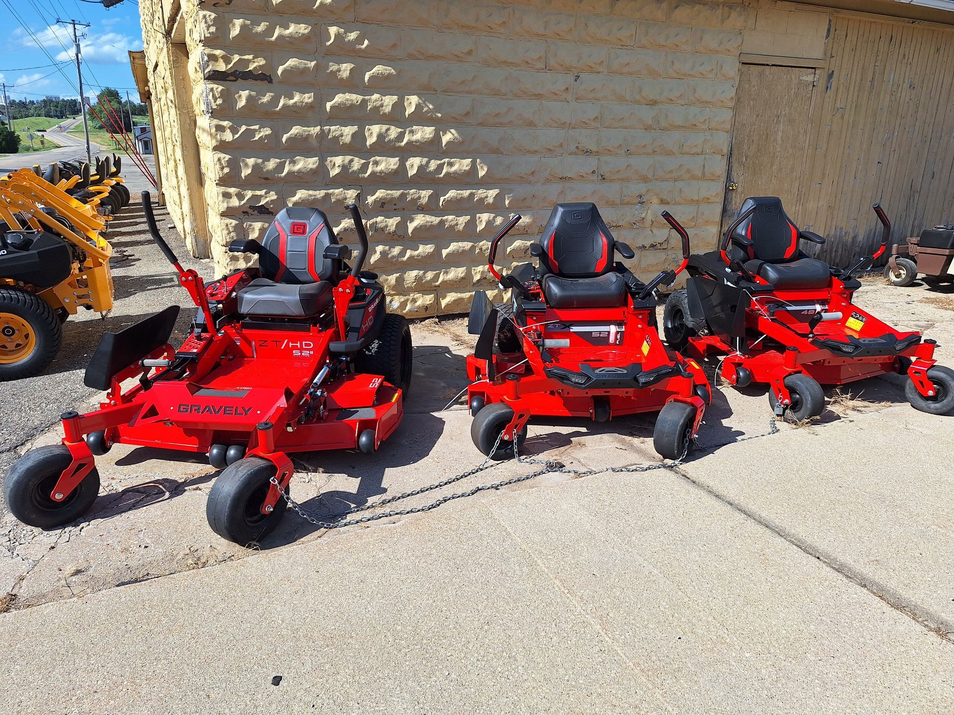 Three red lawn mowers are parked in front of a building.