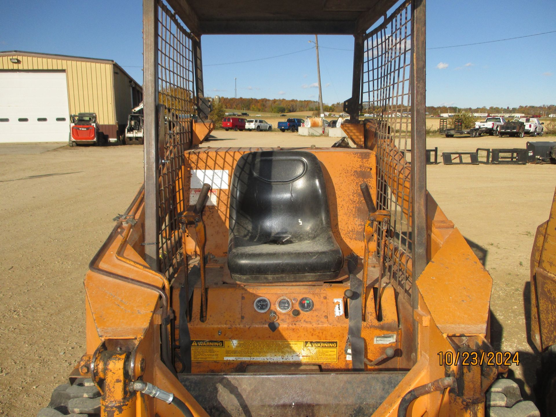A small orange tractor with a black seat is parked in a dirt field.