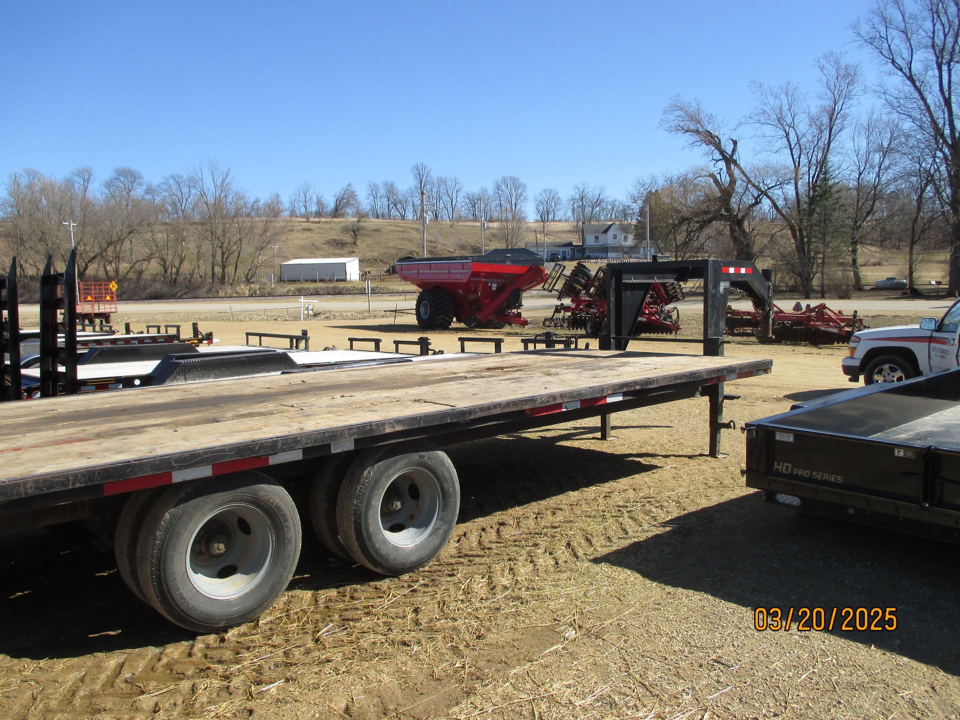 A flatbed trailer is parked in a dirt lot next to a truck.