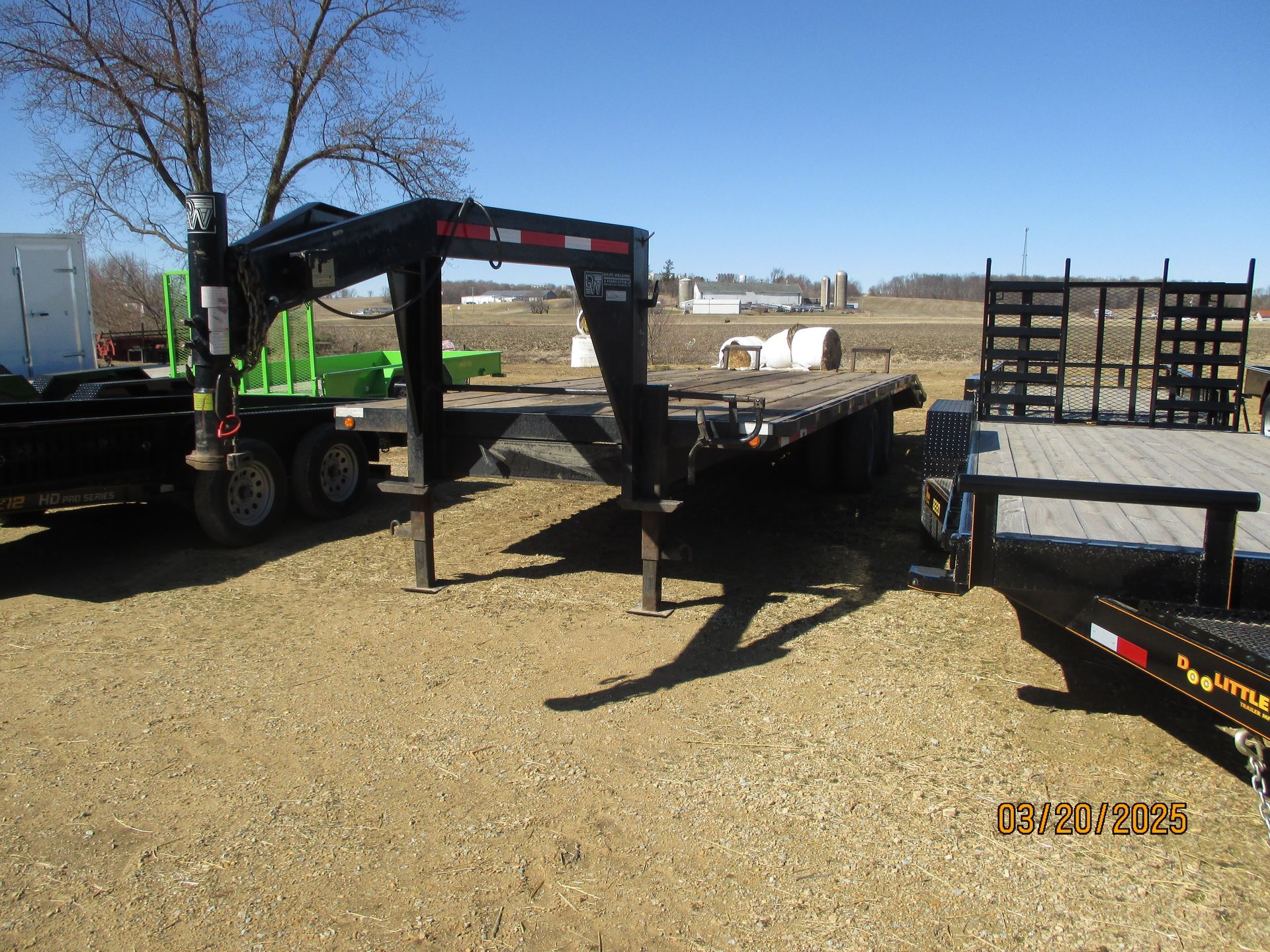 A trailer with a crane attached to it is parked in a gravel lot.