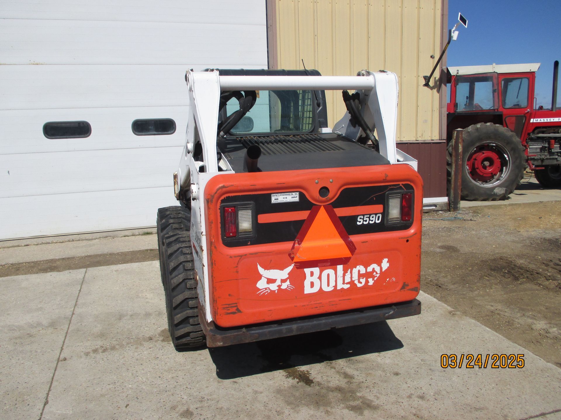 A bobcat skid steer is parked in front of a garage.