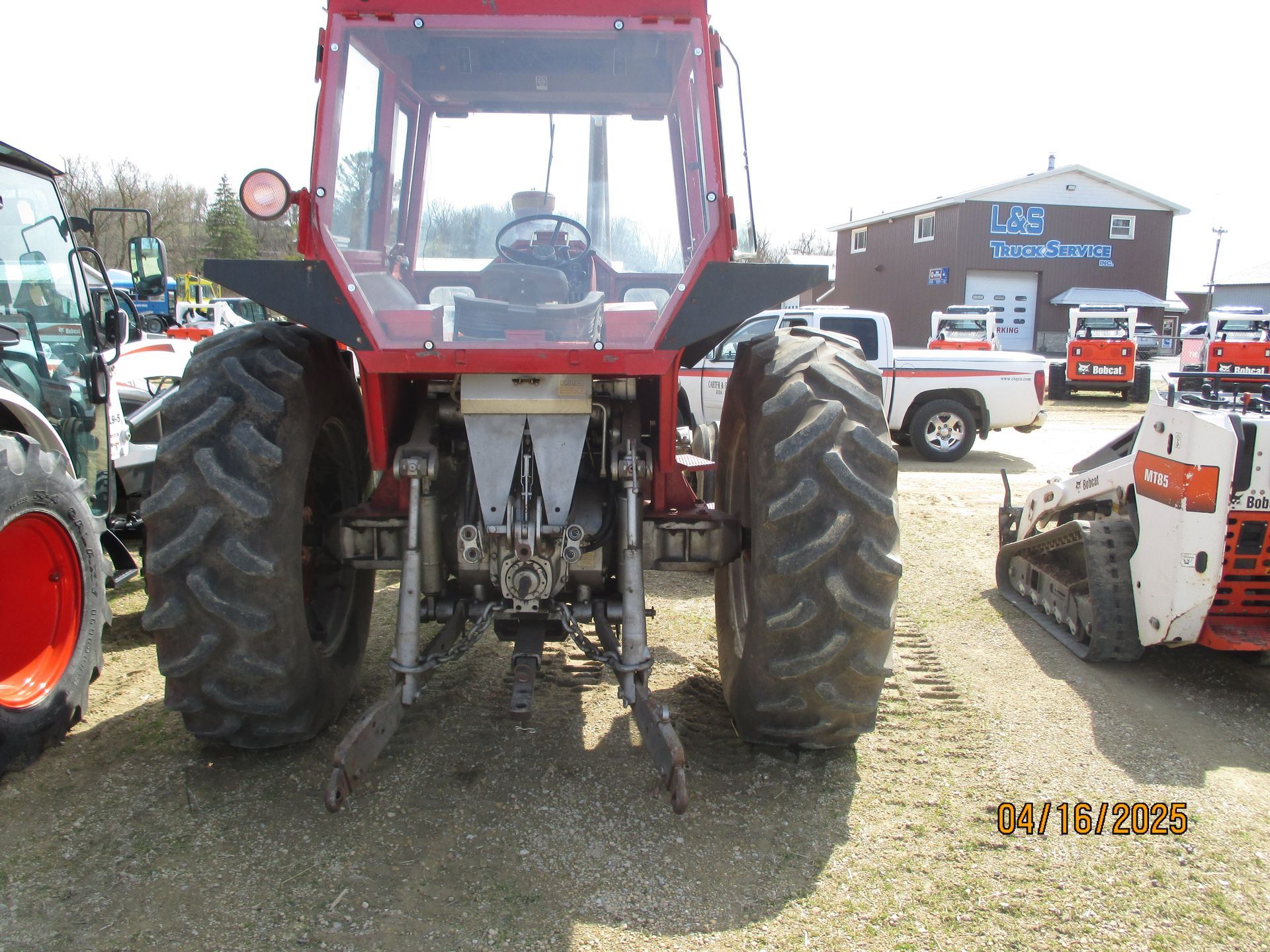 A red tractor is parked in a lot with other tractors.
