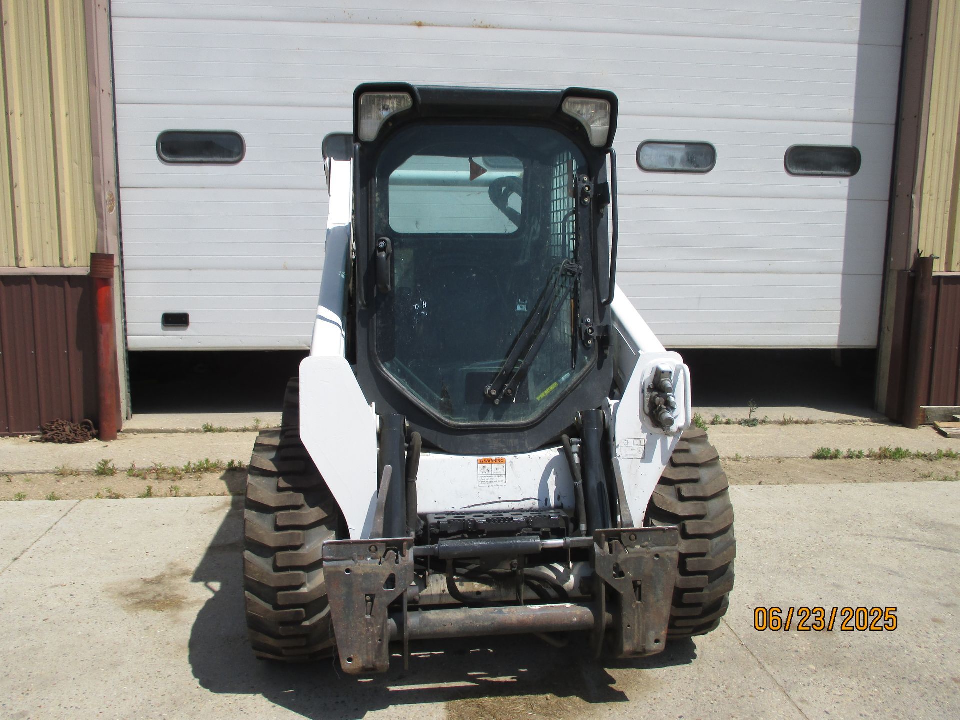 A bobcat is parked in front of a garage door