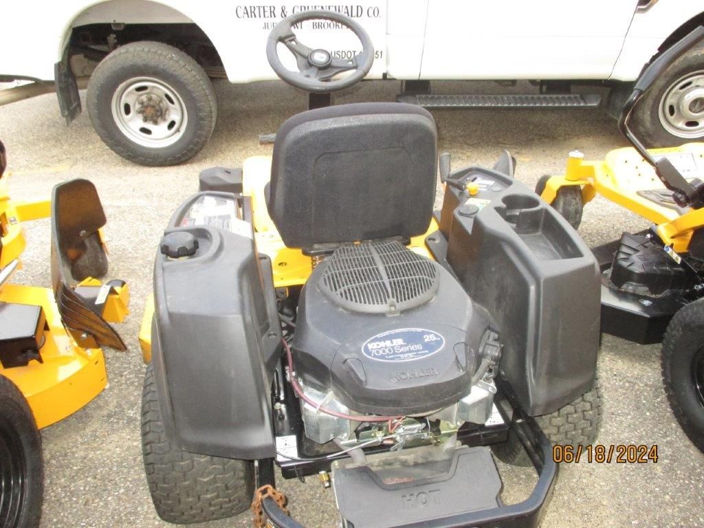 A yellow and black lawn mower is parked next to a white truck.