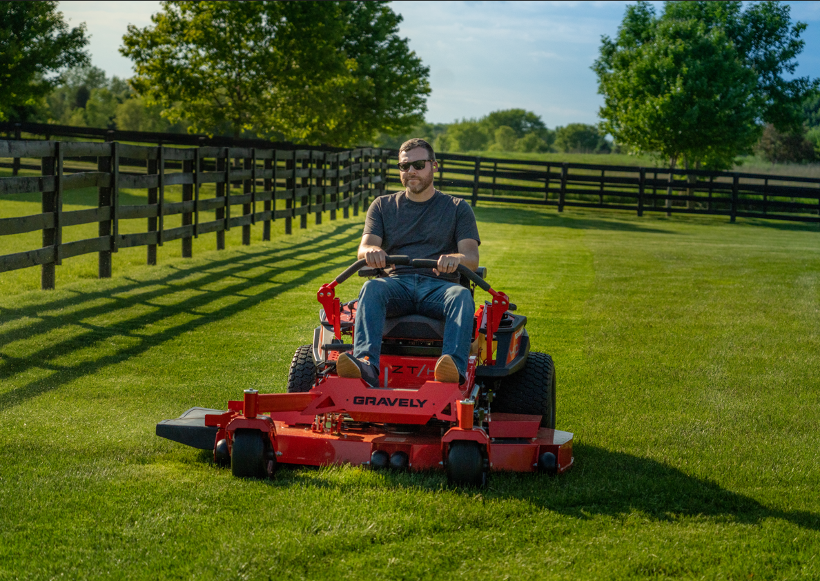 A man is riding a red lawn mower on a lush green lawn.