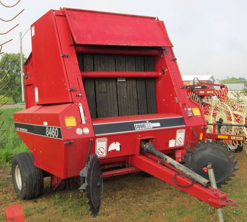A red hay baler is parked in a grassy field