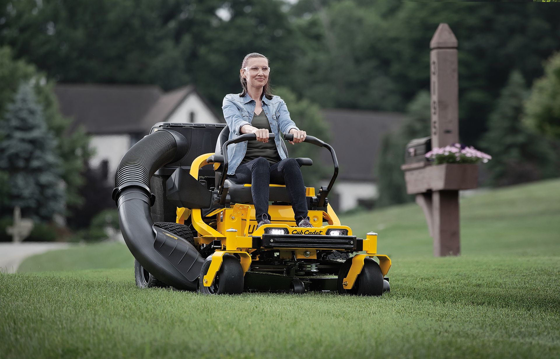 A woman is riding a yellow lawn mower on a lush green lawn.