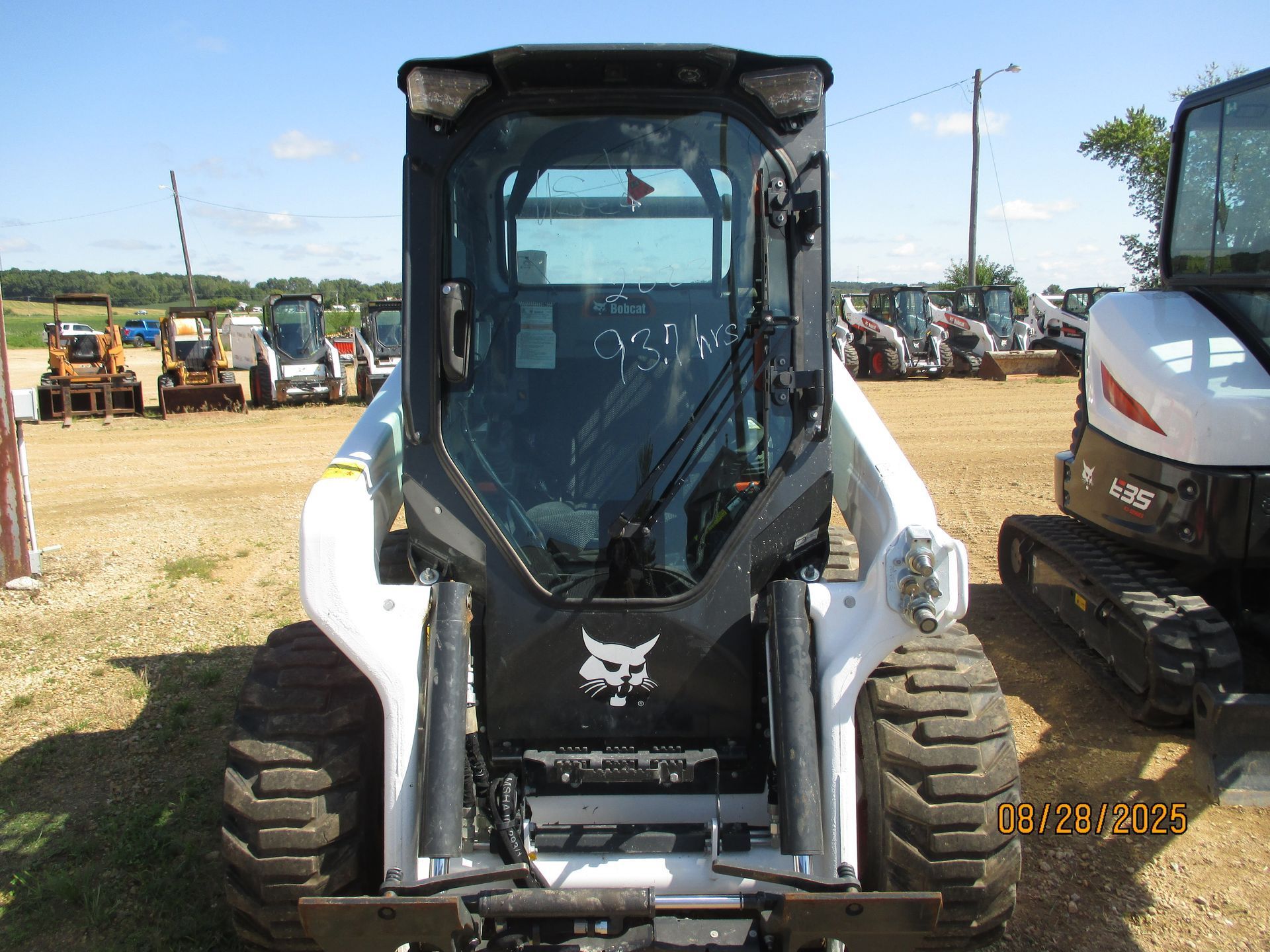 Front view of a Bobcat skid-steer loader with a glass cab, parked on a sunny day.