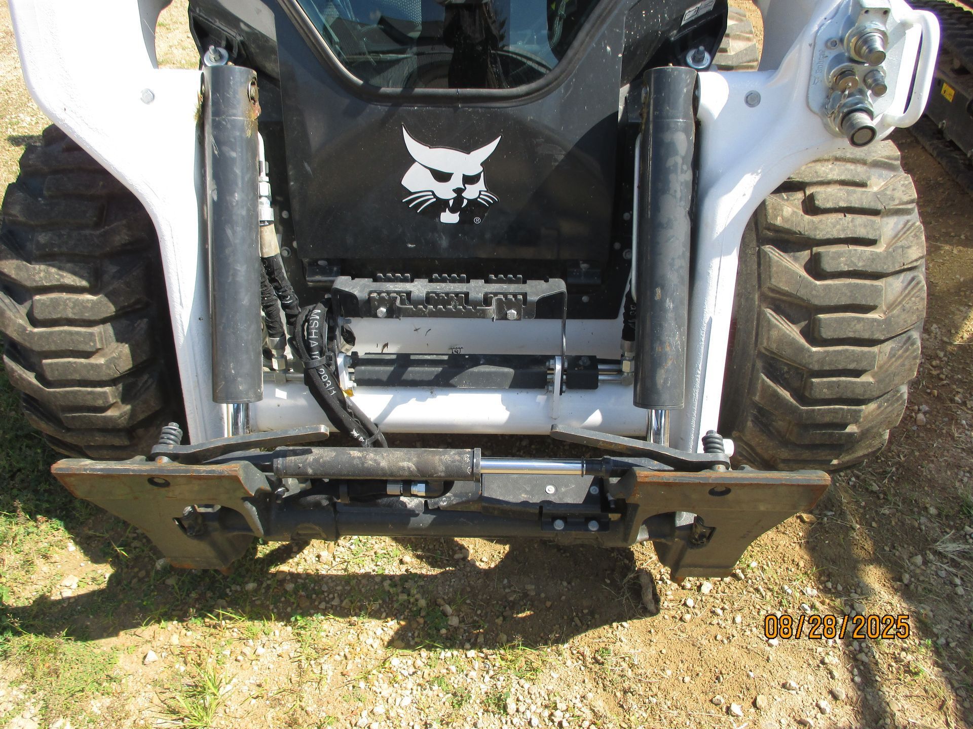 Front view of a Bobcat skid steer loader with a coupler, parked outdoors on grass.
