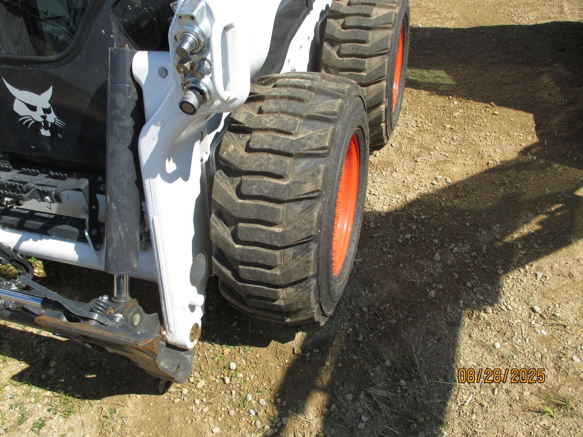 A white Bobcat skid-steer loader, showing the tire and front structure, parked on dirt.
