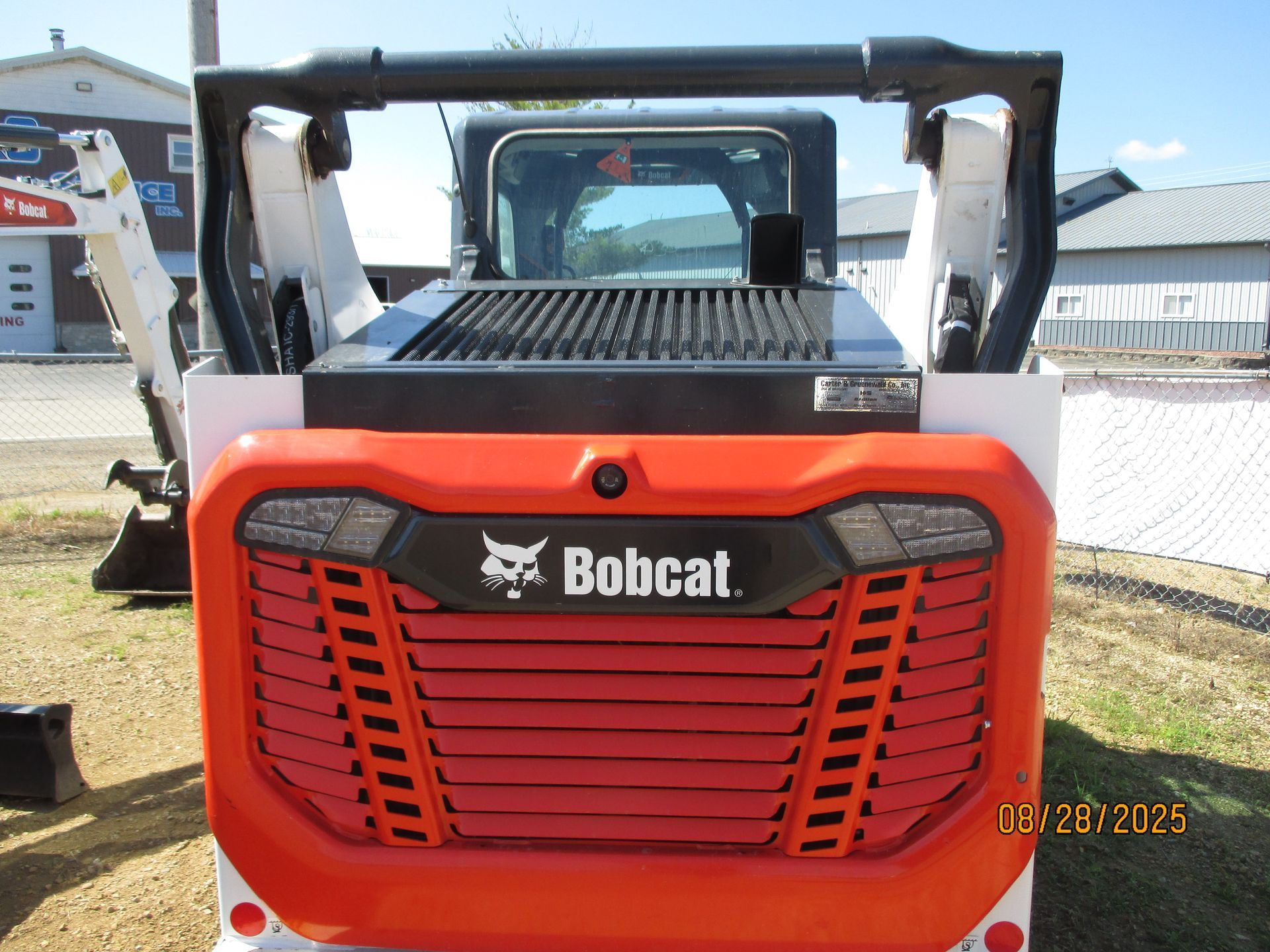 Rear view of a red and white Bobcat skid-steer loader with the Bobcat logo, parked outside.