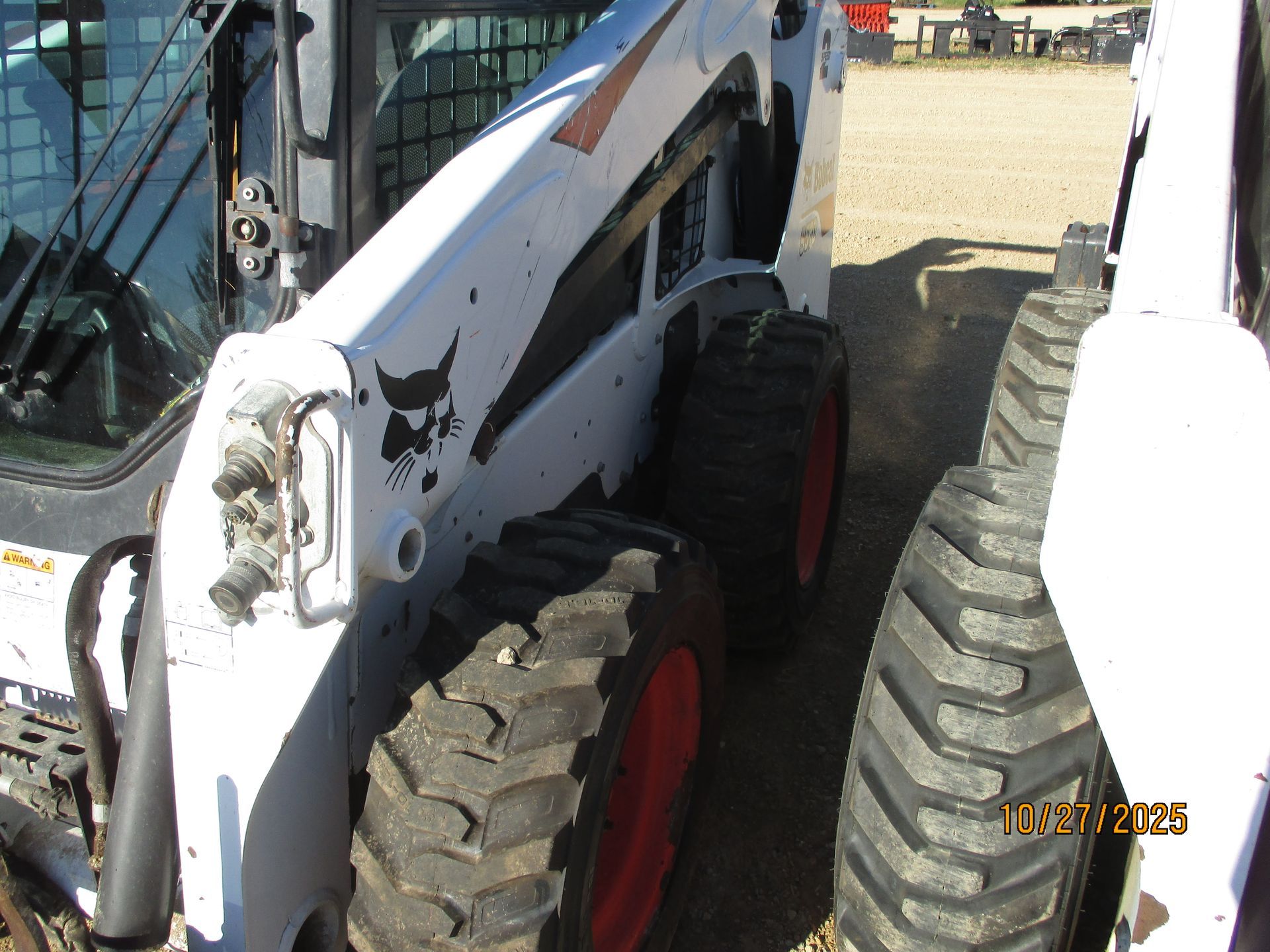 White Bobcat skid-steer loader parked outdoors, showing wheels and arm.