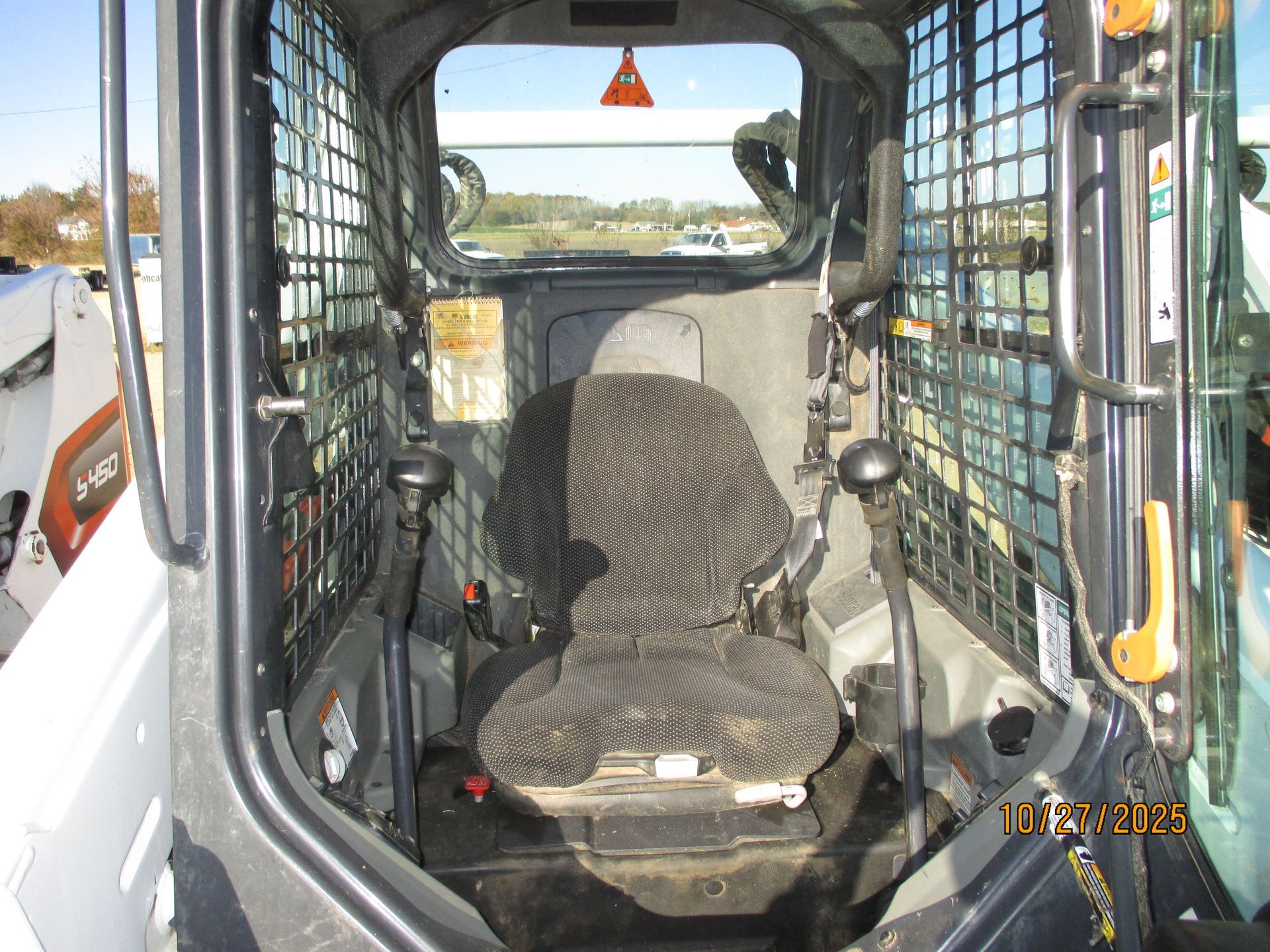 Interior view of a Bobcat skid-steer loader cab, showing the operator's seat, controls, and safety cage.
