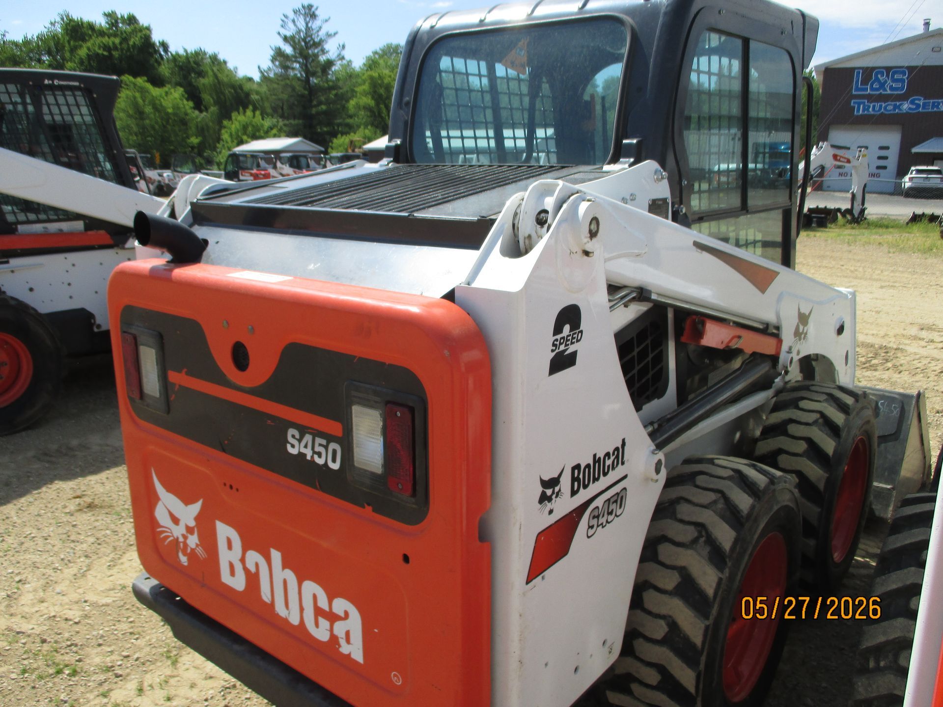 White and orange Bobcat skid-steer loader parked outdoors on gravel.