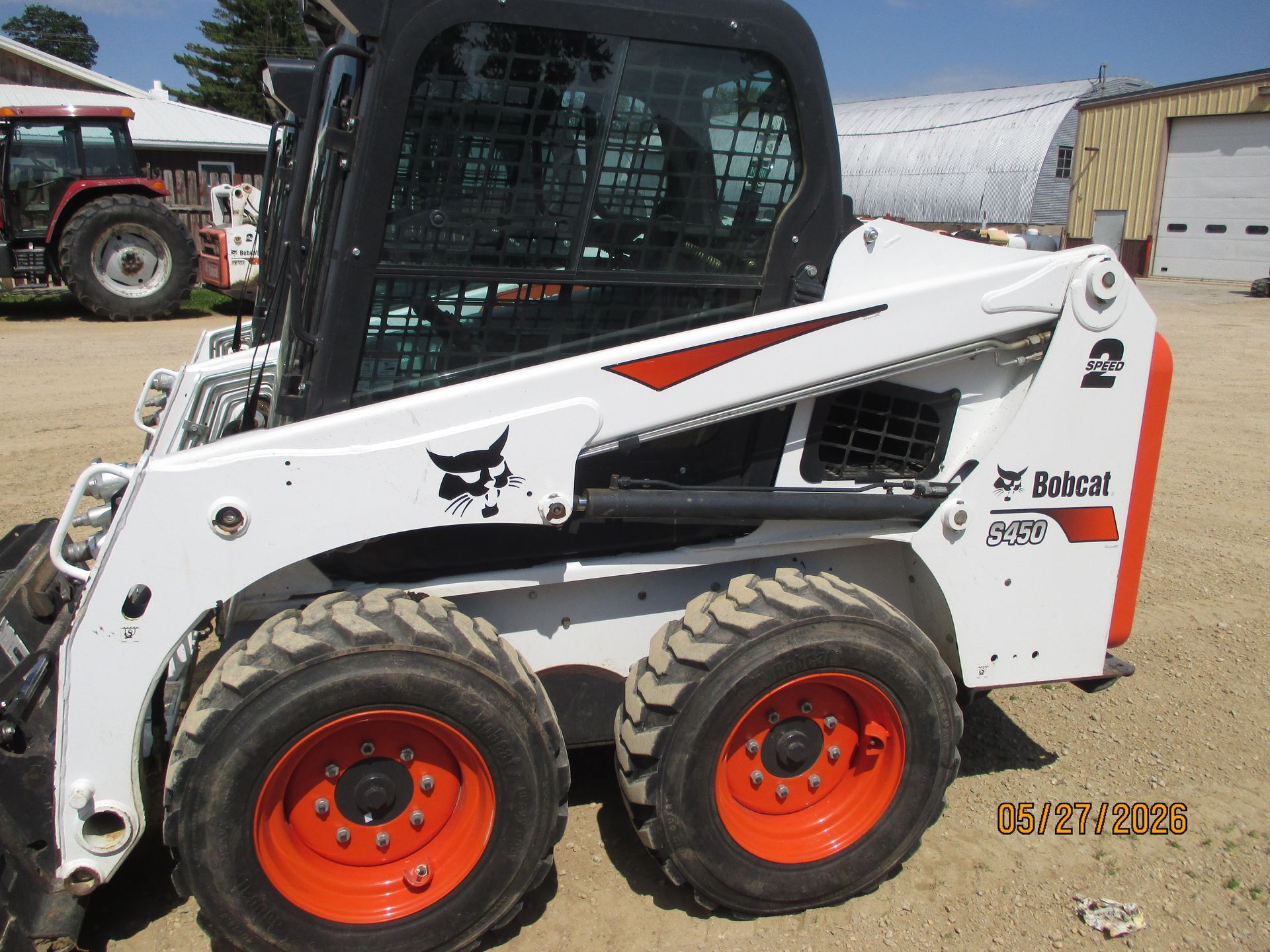 White and orange skid steer loader parked outdoors at a construction yard