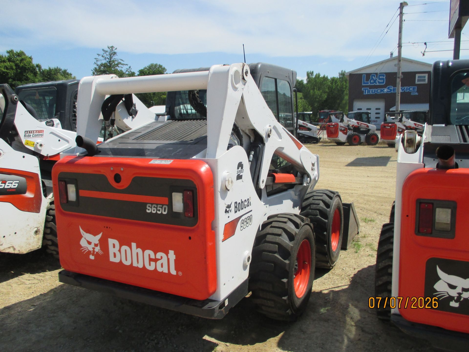 Bobcat skid-steer loader at an outdoor equipment lot, red and white with a rear view.