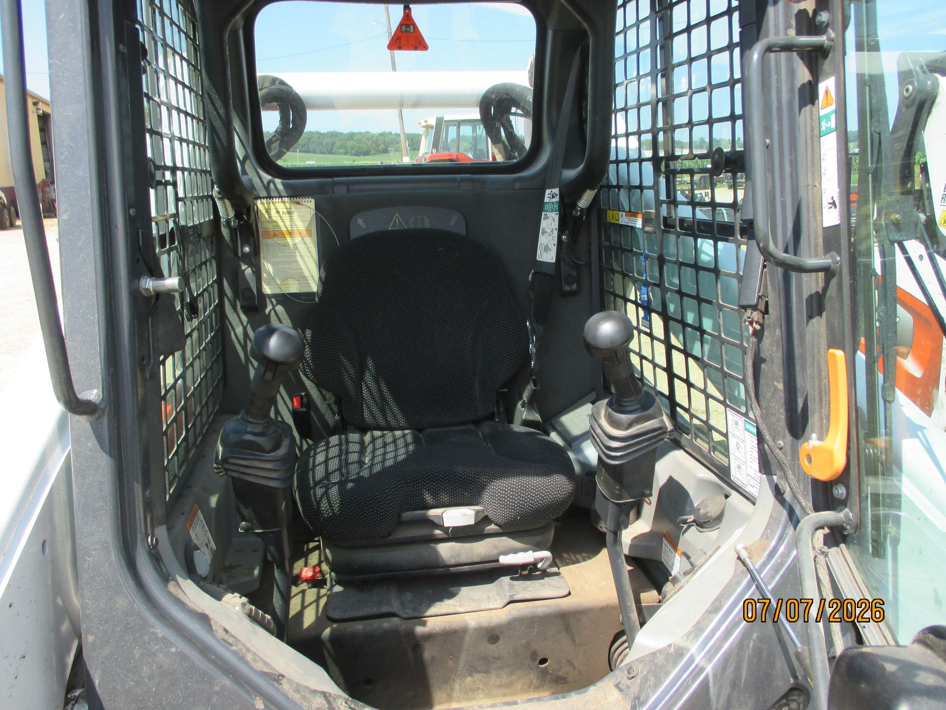 Interior of a construction vehicle cab with black seat, control joysticks, and metal safety cage framing the windows.