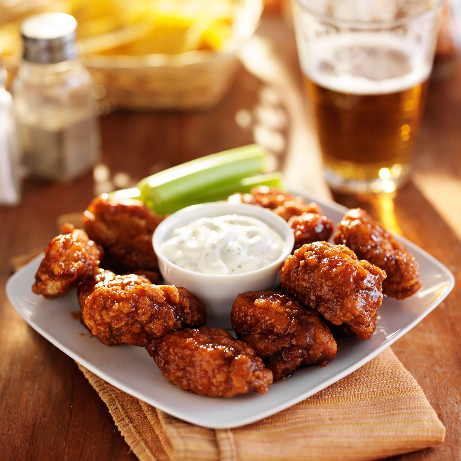 Plate of crispy chicken wings with dip, celery, and beer.