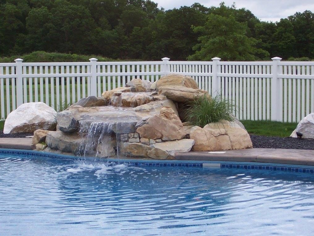 A swimming pool with a waterfall and a white fence