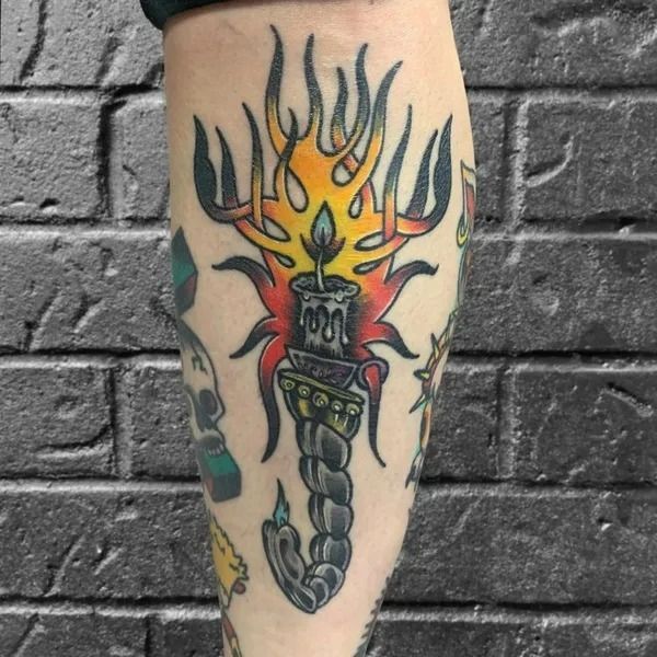 Tattoo of a candle burning with flames, on a leg. Traditional style. Against a brick wall.