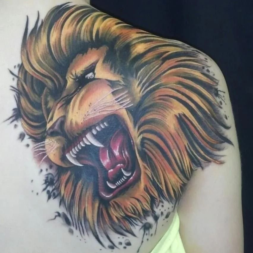 Lion head tattoo on a shoulder. Angry expression with open mouth, showing teeth. Orange and yellow colors.