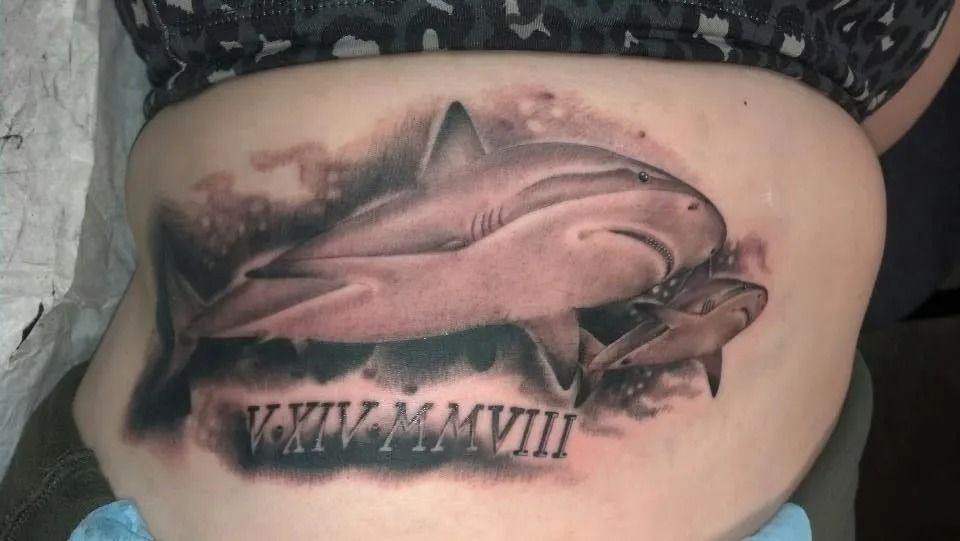 Tattoo of two sharks, a large one and a smaller one, with roman numerals below, on a person's torso.