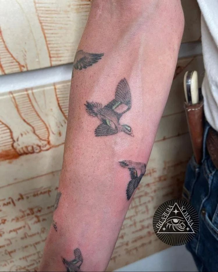Tattoo of several birds in flight on a person's arm.  A drawing of anatomy is in the background.