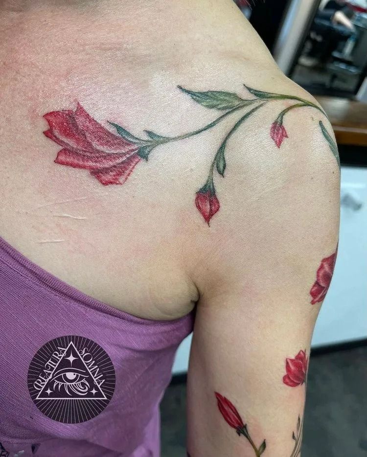 Red flower tattoo on a shoulder and arm, with green leaves and buds, purple tank top visible.