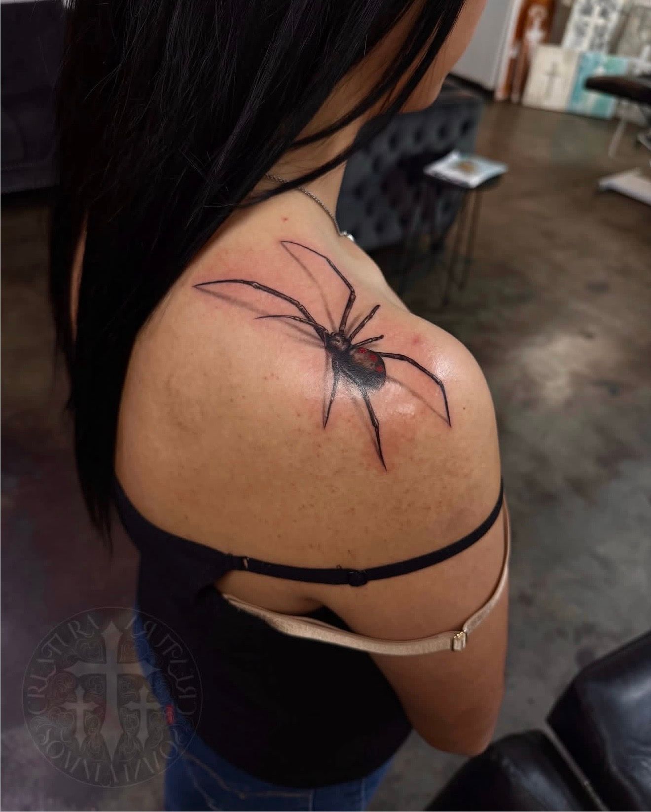 Spider tattoo on upper back and shoulder of a person in a black top.
