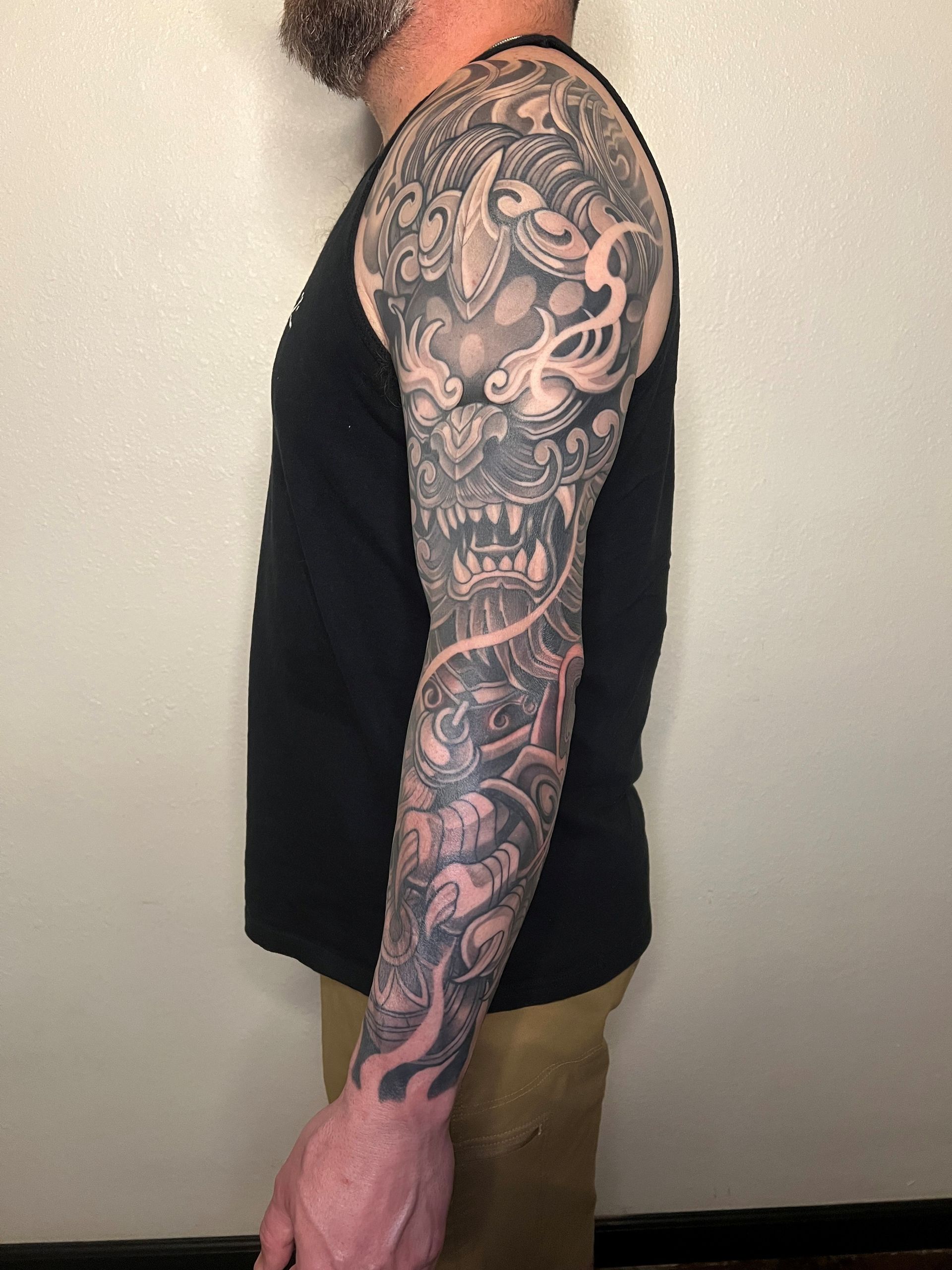 Man with a full-sleeve tattoo of a detailed, intricate dragon design; wearing a black tank top.