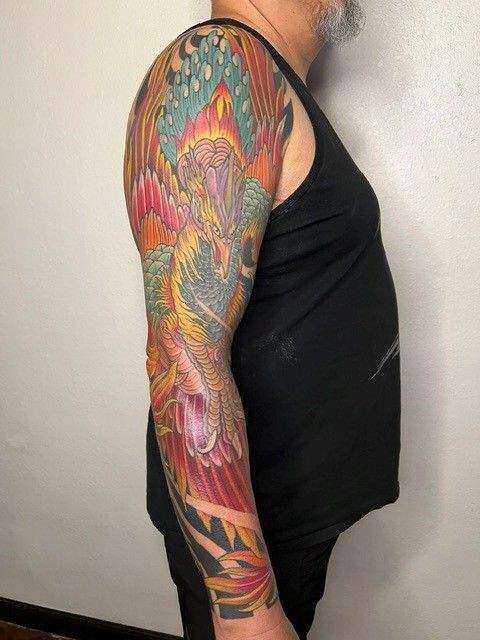 Colorful phoenix tattoo on a man's arm; wearing a black tank top.