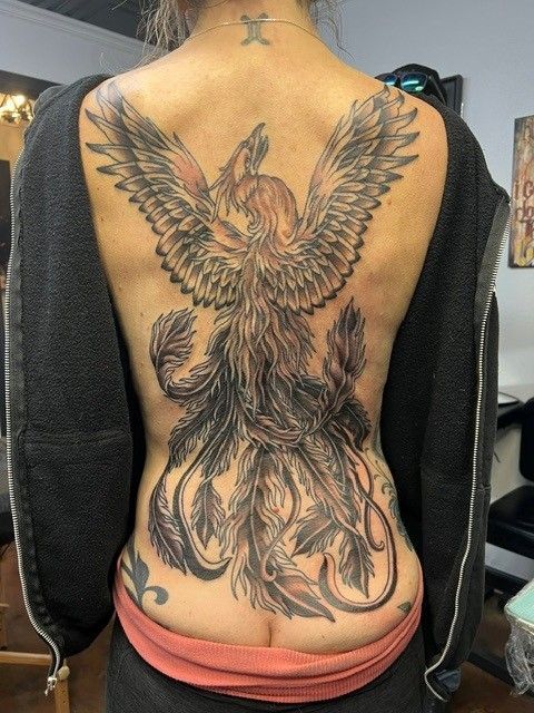 Full back tattoo of a phoenix with outstretched wings, in shades of black and red, on a person’s back.