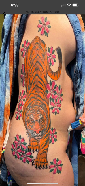 A person's side with a tiger and pink flower tattoos. The tiger is orange and black.