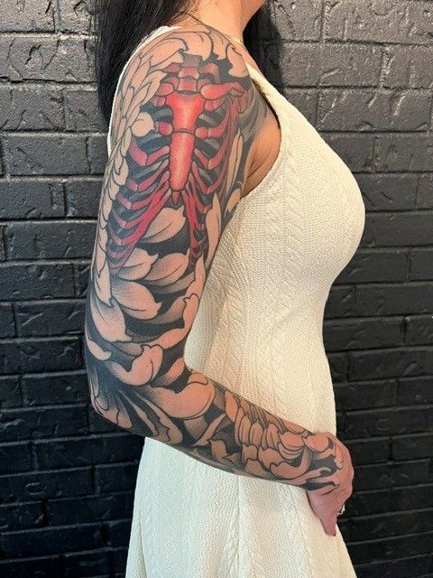 Woman with full arm tattoo of rib cage and flowers, in a white dress.