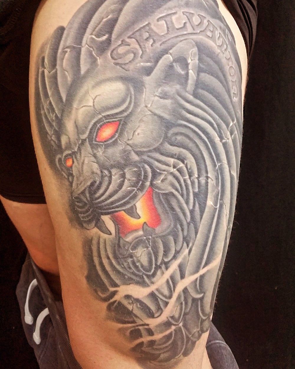 Tattoo of a stone lion with glowing red eyes on a thigh.
