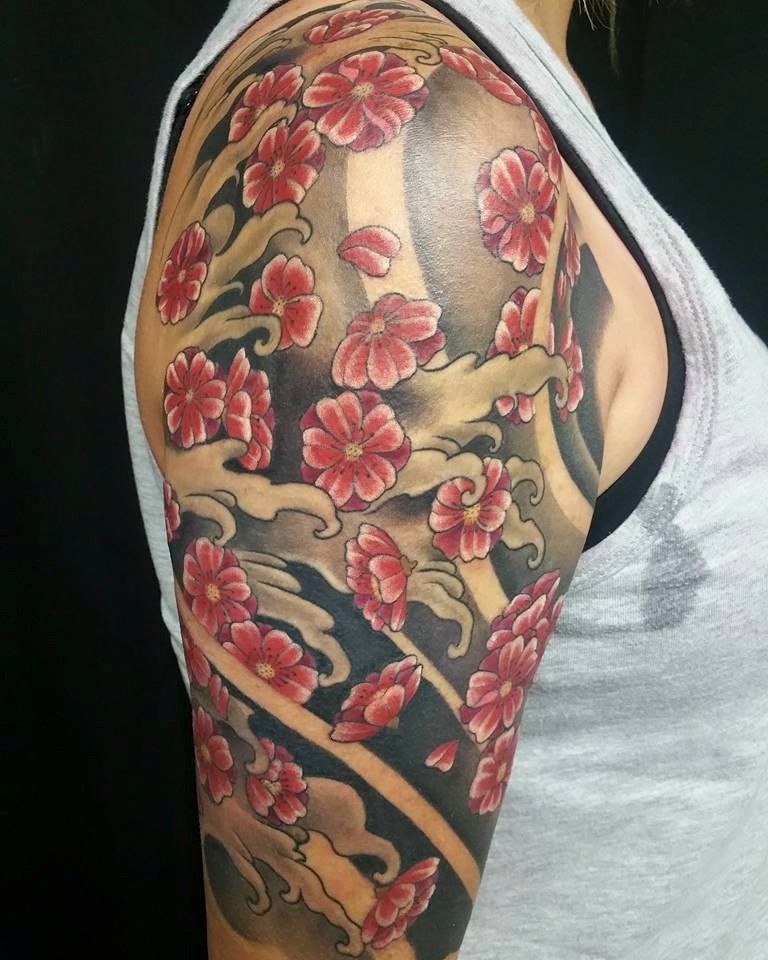 Tattoo of red cherry blossoms and gray clouds on a woman's arm, over a black background.