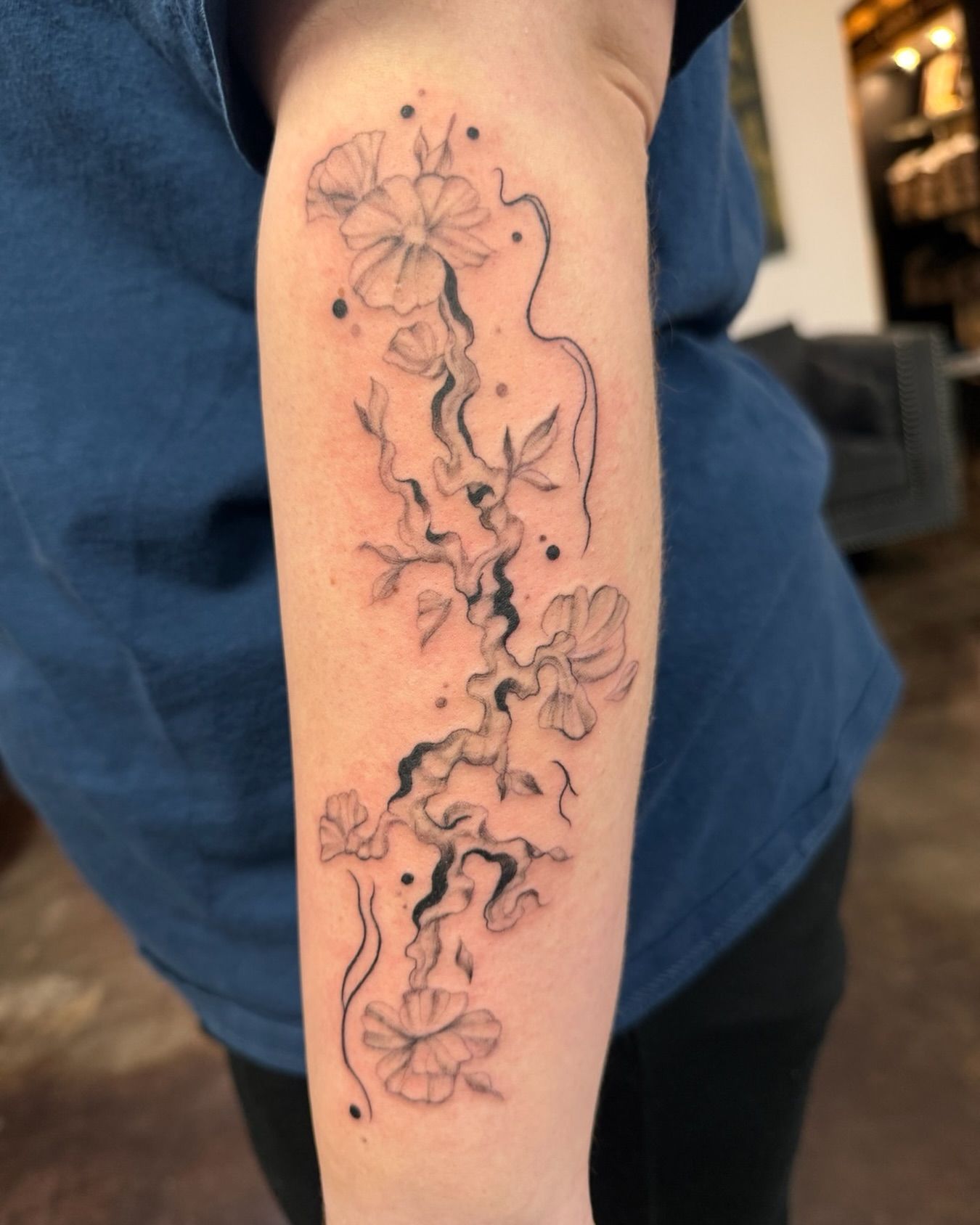 Tattoo of a black ink vine with flowers on an arm.