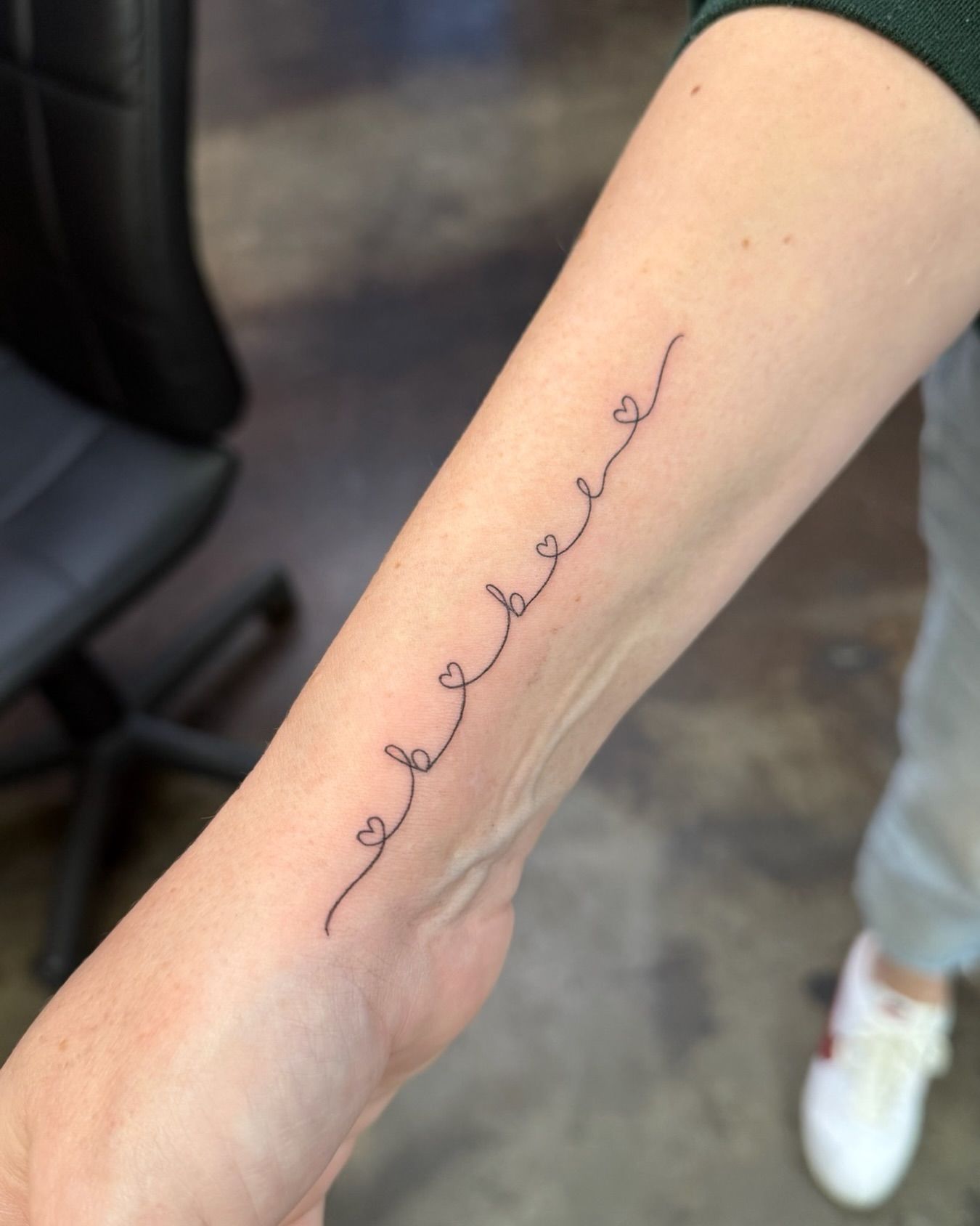 Arm with a wrist tattoo: connected hearts, delicate line art.