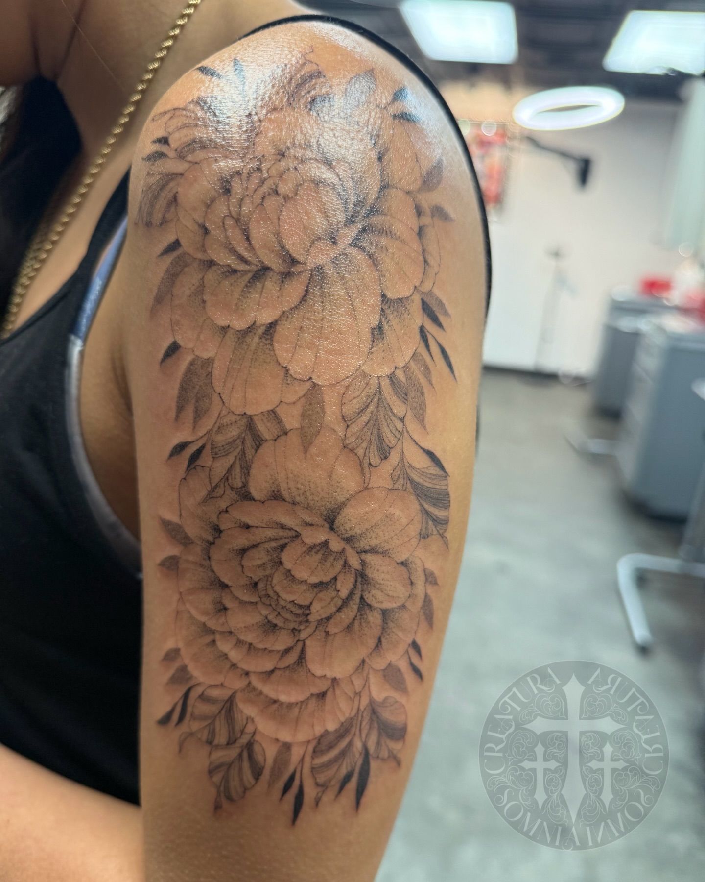 Tattoo of detailed peony flowers cascading down a person's upper arm. Black and gray shading. Studio background.