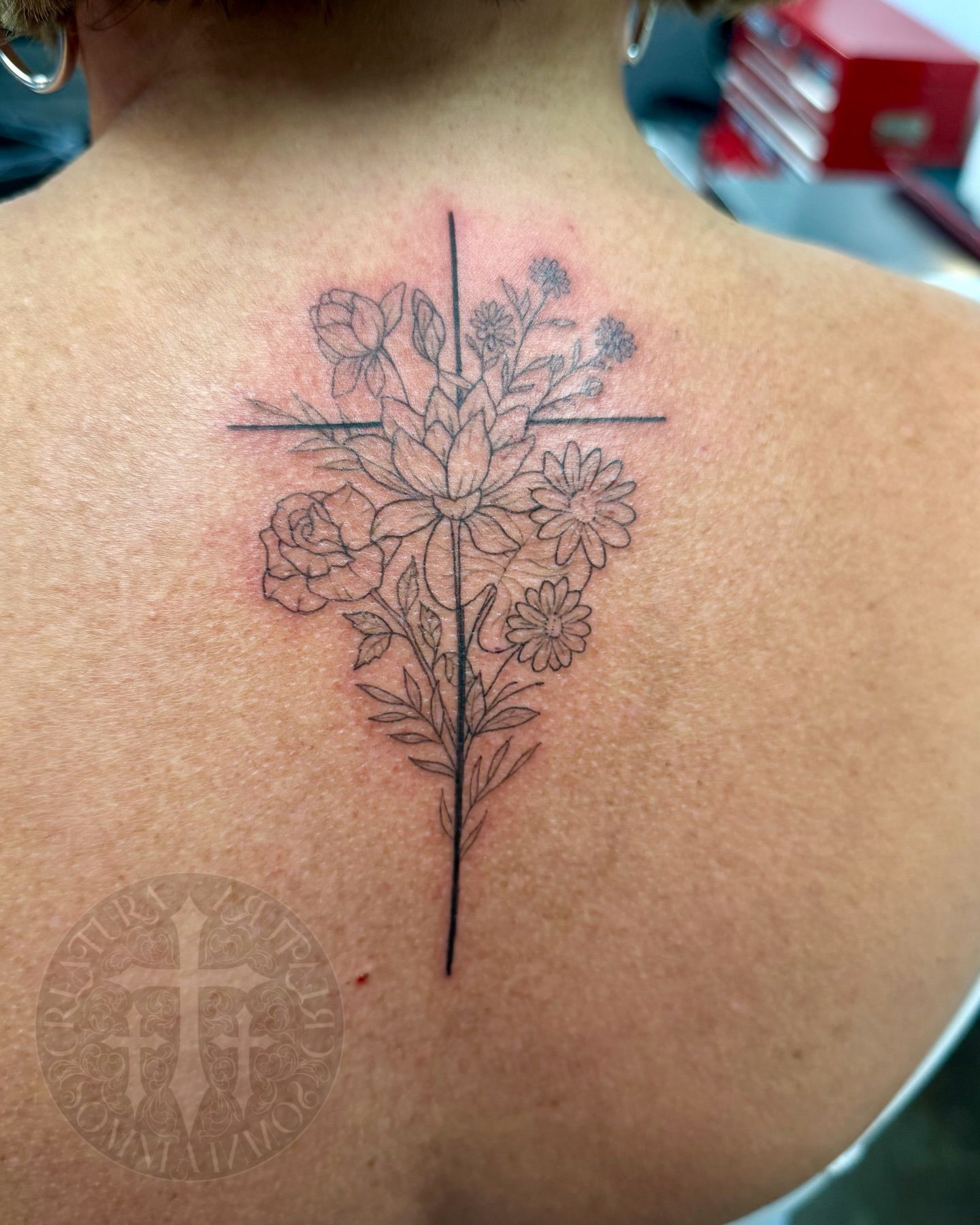 Cross tattoo with floral bouquet on upper back.